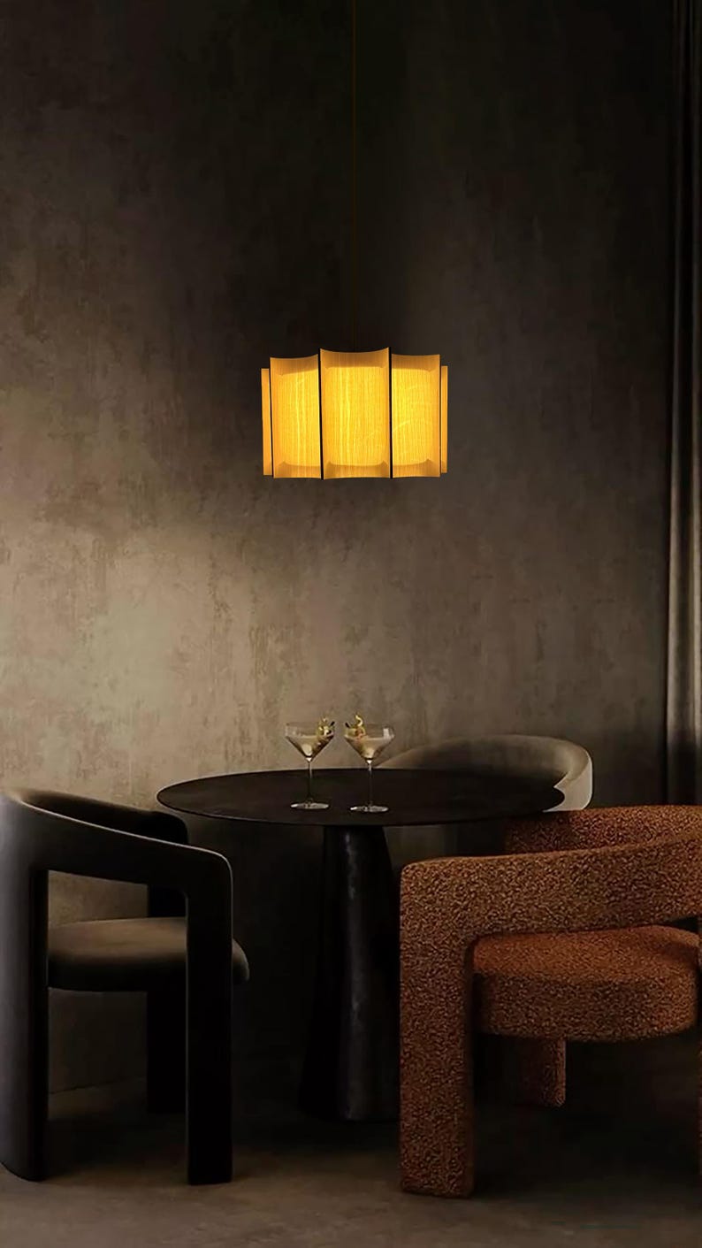 May include: A modern interior scene featuring a rectangular, illuminated light fixture with a warm, yellow glow. Below, a dark round table is set with two martini glasses. The scene includes dark chairs with unique designs, creating a sophisticated ambiance.