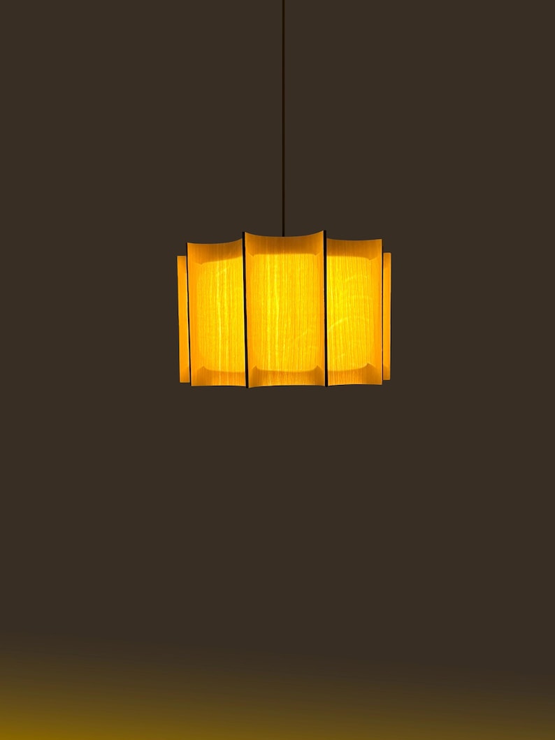 May include: A modern pendant light fixture with a rectangular shade. The shade is made of vertical wooden slats with a warm yellow glow emanating from within. The fixture hangs from a thin black cord against a dark brown background.