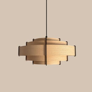 Puede incluir: Una l&aacute;mpara colgante moderna de madera con un dise&ntilde;o en capas. La l&aacute;mpara presenta listones horizontales de madera y detalles en metal oscuro. Cuelga de un cable negro, ofreciendo una est&eacute;tica minimalista y contempor&aacute;nea.