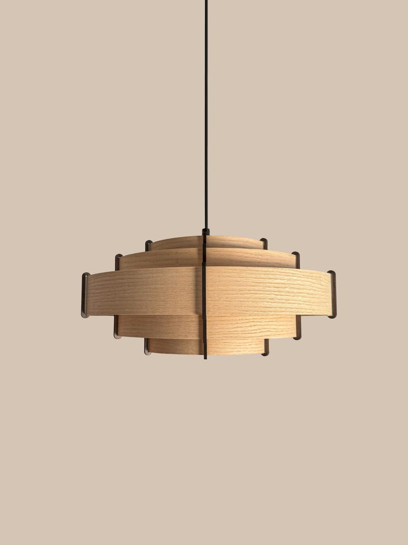 Puede incluir: Una l&aacute;mpara colgante moderna de madera con un dise&ntilde;o en capas. La l&aacute;mpara presenta listones horizontales de madera y detalles en metal oscuro. Cuelga de un cable negro, ofreciendo una est&eacute;tica minimalista y contempor&aacute;nea.