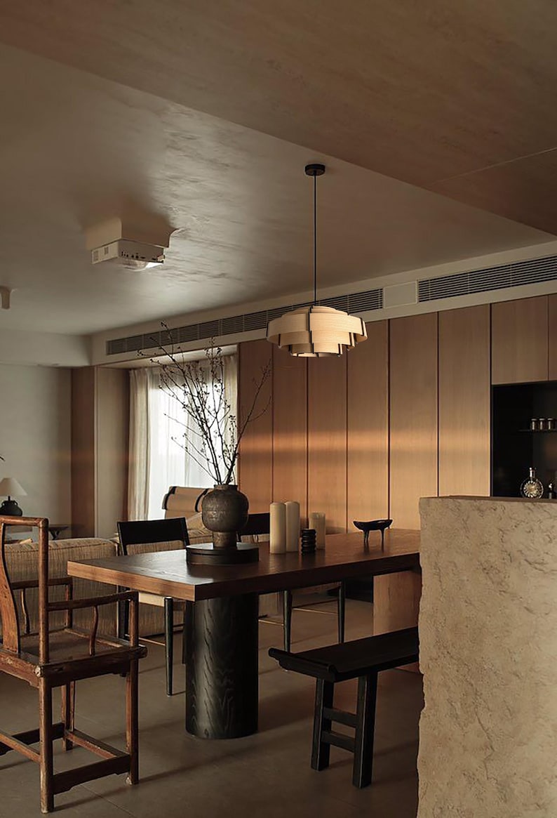 Puede incluir: Un comedor con una mesa de madera oscura, un banco negro y sillas de madera. Una l&aacute;mpara decorativa cuelga sobre la mesa. Un jarr&oacute;n con ramas y velas est&aacute; sobre la mesa. Las paredes son de paneles de madera.