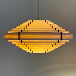 May include: A modern, geometric pendant light fixture. The light is constructed from layered wooden slats, creating a tiered, diamond-like shape. The warm, yellow light emanates from within, and is suspended by a black cord.
