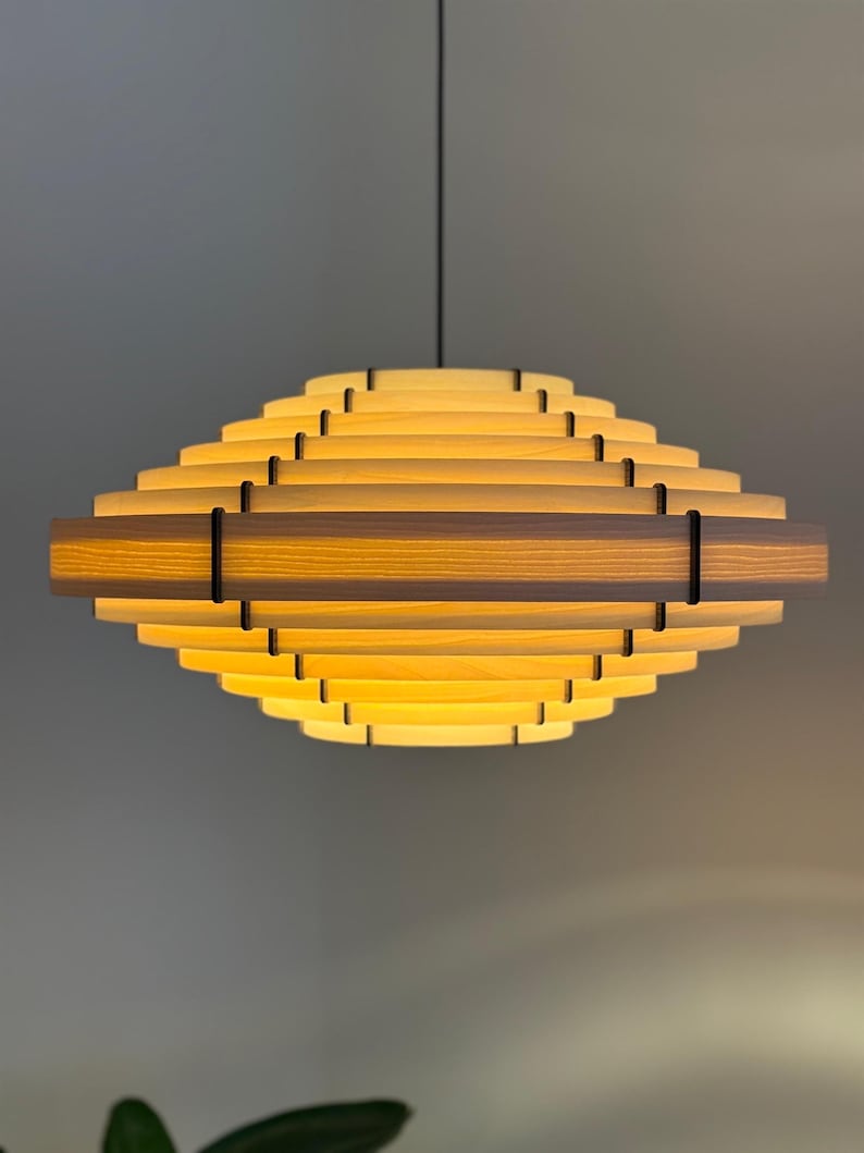 May include: A modern, geometric pendant light fixture. The light is constructed from layered wooden slats, creating a tiered, diamond-like shape. The warm, yellow light emanates from within, and is suspended by a black cord.