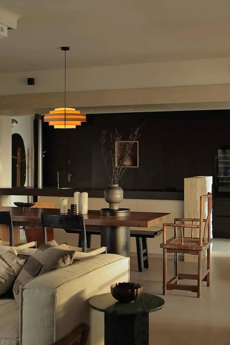 Puede incluir: Vista interior de un espacio habitable moderno con comedor. Una l&aacute;mpara colgante circular escalonada cuelga sobre una mesa de comedor de madera oscura. Tambi&eacute;n se ven un sof&aacute;, una mesa auxiliar y una silla de madera.