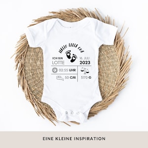 Könnte beinhalten: Weißer Baby-Body mit schwarzem Text: "Hello Little One", der Name "Lotte", Geburtsdatum, Uhrzeit, Länge (50 cm) und Gewicht (3170 g). Der Body liegt auf einer gewebten, kreisförmigen Matte. Der Text unten lautet "EINE KLEINE INSPIRATION."