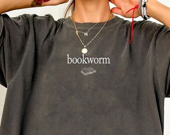 May include: A charcoal gray oversized t-shirt featuring the word bookworm printed in white text on the center chest, accompanied by a small graphic of an open book directly below the text. The shirt has a relaxed fit with short sleeves.
