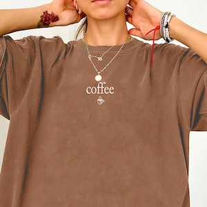May include: Espresso-colored, oversized t-shirt with the word "coffee" printed in white, along with a coffee cup graphic. The shirt has a vintage, washed look and a relaxed fit. The word "Espresso" is written in a script font at the bottom left.