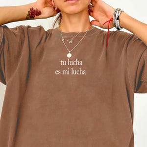 May include: Espresso-colored oversized t-shirt with the text "tu lucha es mi lucha" in white. The shirt has a relaxed fit and short sleeves. The word "Espresso" is written in cursive at the bottom left corner.