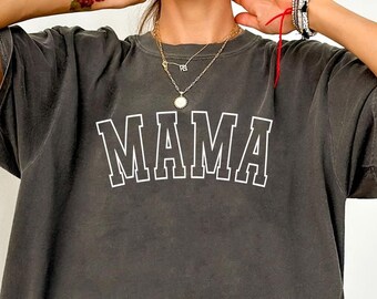 May include: A charcoal gray oversized t-shirt featuring the word MAMA printed in a white collegiate-style font across the chest. The garment has short sleeves, a crew neckline, and a washed-out, vintage-inspired fabric texture throughout.