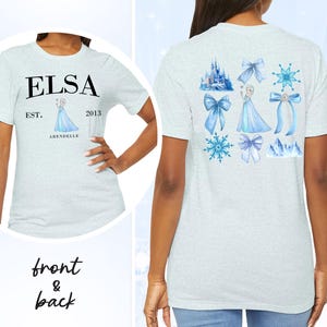 May include: Light gray t-shirt with "ELSA" printed in black, "EST. 2013 ARENDELLE" below, and a watercolor image of Elsa. The back features watercolor images of bows, snowflakes, a castle, and Elsa in a blue dress.