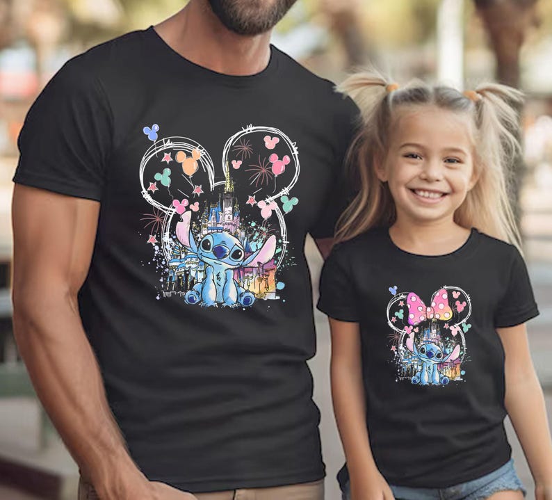 K&ouml;nnte beinhalten: Schwarze T-Shirts mit einer farbenfrohen Grafik der Figur Stitch aus Lilo & Stitch. Das Design umfasst ein Schloss, Feuerwerk und Mickey Mouse Ohren. Die Shirts werden von einem Mann und einem jungen M&auml;dchen getragen.