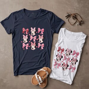 以下が含まれることがあります： ネイビーブルーの半袖Tシャツとホワイトのノースリーブタンクトップ。どちらもミニーマウスの顔、ピンクのリボン、小さなハートが繰り返されるパターンがプリントされています。セットにはブラウンのサンダルと縁なし眼鏡が添えられています。