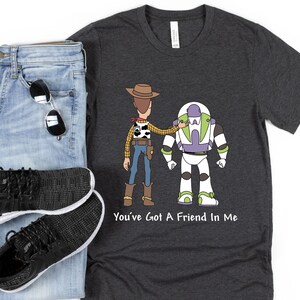 Puede incluir: Una camiseta gris oscuro con una imagen de dibujos animados de Woody y Buzz Lightyear de Toy Story. El texto "You've Got A Friend In Me" est&aacute; impreso debajo de la imagen.