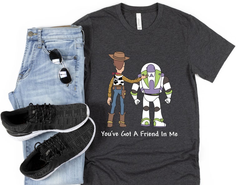 Puede incluir: Una camiseta gris oscuro con una imagen de dibujos animados de Woody y Buzz Lightyear de Toy Story. El texto "You've Got A Friend In Me" est&aacute; impreso debajo de la imagen.