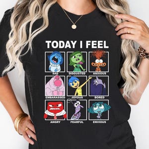 Pu&ograve; includere: Maglietta nera con il testo "TODAY I FEEL" e una griglia di nove personaggi dei cartoni animati che rappresentano diverse emozioni. I personaggi sono del film Inside Out. Le emozioni includono tristezza, disgusto, ansia, imbarazzo, gioia, noia, rabbia, paura e invidia.