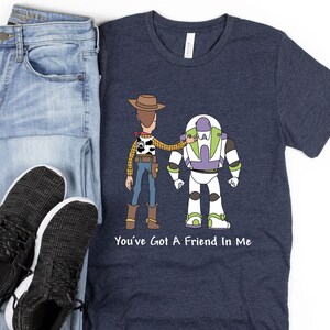 Puede incluir: Una camiseta azul marino con una imagen de dibujos animados de Woody y Buzz Lightyear de Toy Story. El texto "You've Got A Friend In Me" est&aacute; impreso debajo de la imagen.