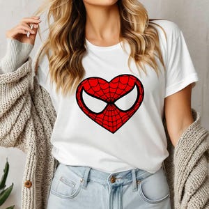 May include: White t-shirt with a red heart-shaped design featuring a black spider web and eyes.
