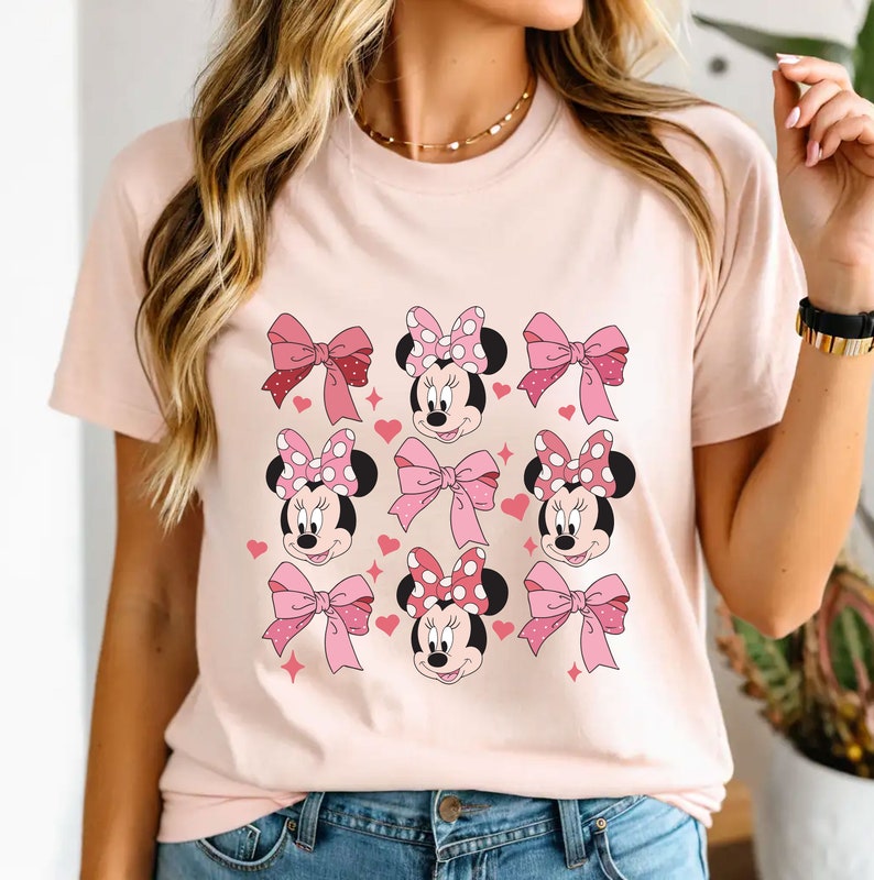May include: Pink t-shirt with a repeated pattern of Minnie Mouse heads wearing pink bows with white polka dots.