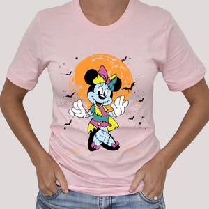 May include: Pink t-shirt featuring a cartoon image of a zombie Minnie Mouse in front of a yellow and orange moon. The image has a Halloween theme.
