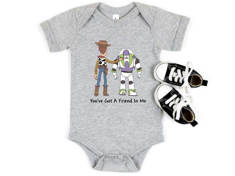 Puede incluir: Un body de beb&eacute; gris con una imagen de dibujos animados de Woody y Buzz Lightyear de Toy Story. El body tiene el texto "You've Got A Friend In Me" impreso en &eacute;l.