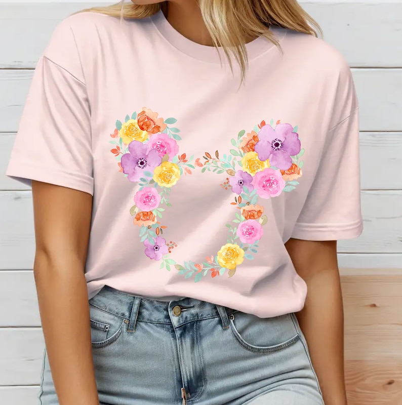 May include: A pink t-shirt with a floral Mickey Mouse design. The flowers are in shades of yellow, orange, pink, and purple.