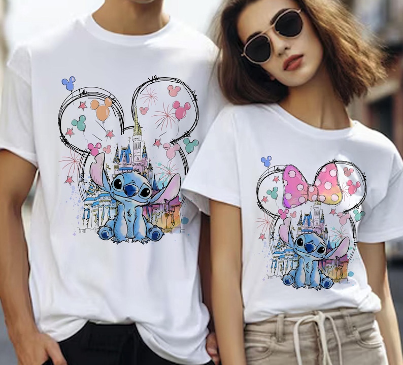 K&ouml;nnte beinhalten: Wei&szlig;e T-Shirts mit einem Stitch-Cartoon-Design. Das Design umfasst ein Schloss, Feuerwerk und Mickey Mouse Ohren. Die Stitch-Figur ist blau und die Ohren haben farbige Akzente.