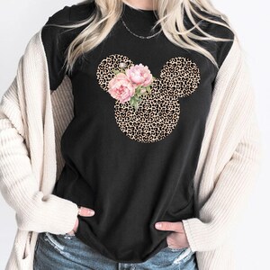 May include: Black t-shirt featuring a Mickey Mouse head design with a leopard print pattern. The design includes pink floral accents. The shirt is a casual wear item.