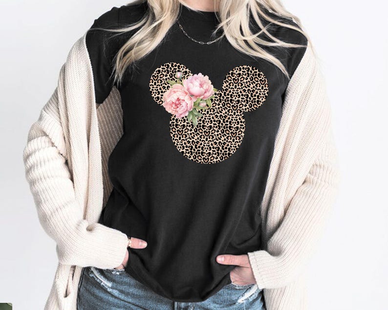 May include: Black t-shirt featuring a Mickey Mouse head design with a leopard print pattern. The design includes pink floral accents. The shirt is a casual wear item.