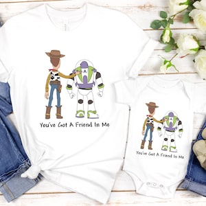 Puede incluir: Dos camisetas blancas con una imagen de dibujos animados de Woody y Buzz Lightyear de Toy Story. El texto "You've Got A Friend In Me" est&aacute; impreso en ambas camisetas.