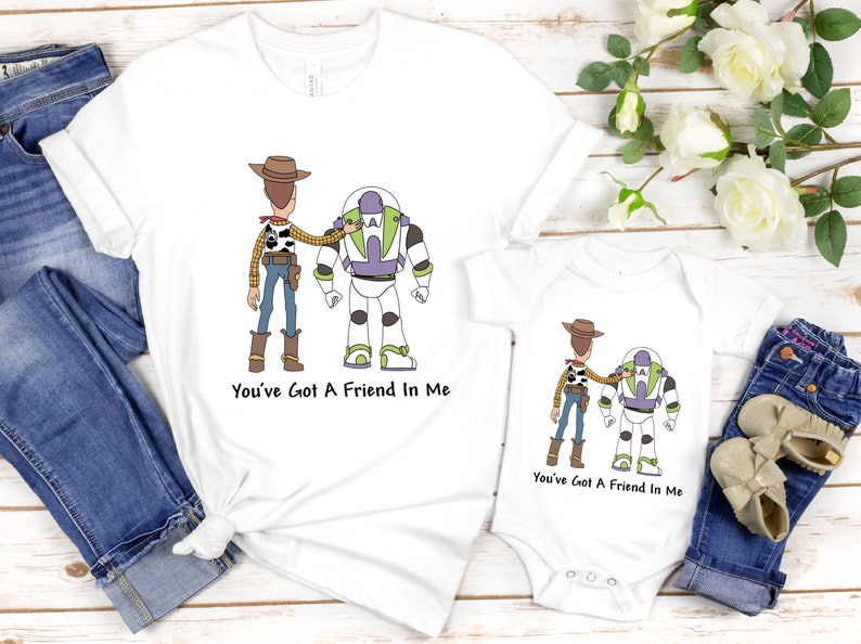 Puede incluir: Dos camisetas blancas con una imagen de dibujos animados de Woody y Buzz Lightyear de Toy Story. El texto "You've Got A Friend In Me" est&aacute; impreso en ambas camisetas.