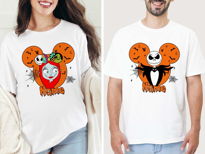 Op de afbeelding: Twee witte T-shirts met een Halloween Mickey Mouse-ontwerp. E&eacute;n shirt heeft Sally van The Nightmare Before Christmas en de andere heeft Jack Skellington. Beide shirts hebben de tekst "Name" onder het ontwerp gedrukt.
