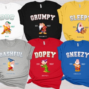 May include: Six different t-shirts featuring the seven dwarfs from Snow White. Each shirt has a different dwarf's name and image, with the text "EST. 1937" below the image. The shirts are in various colors, including white, black, yellow, gray, red, and blue.