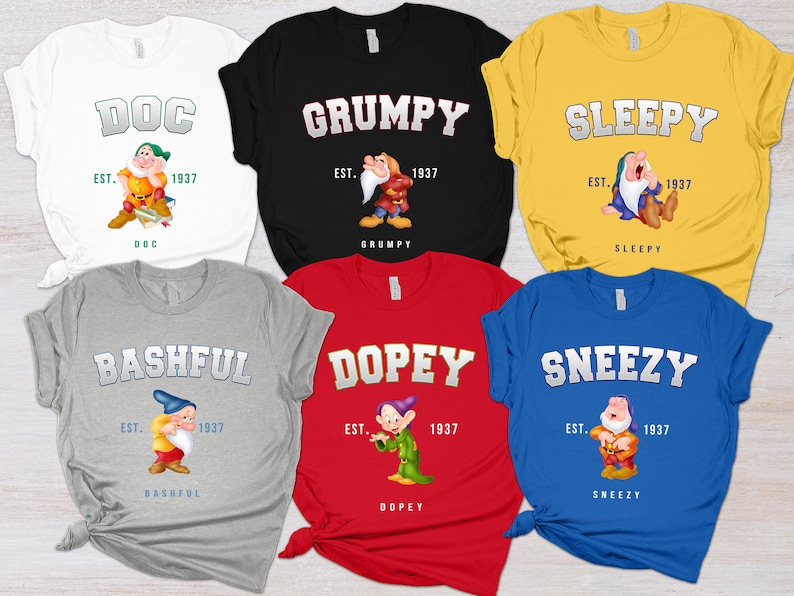 May include: Six different t-shirts featuring the seven dwarfs from Snow White. Each shirt has a different dwarf's name and image, with the text "EST. 1937" below the image. The shirts are in various colors, including white, black, yellow, gray, red, and blue.
