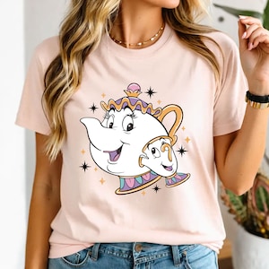 May include: A pink t-shirt with a cartoon image of Mrs. Potts and Chip from Beauty and the Beast. The image is in a white outline with purple, yellow, and gold accents. There are gold stars around the image.
