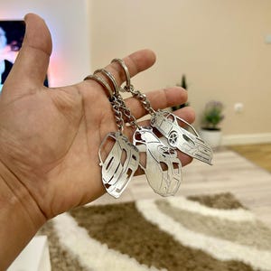 May include: Four silver car keyrings with a detailed outline of a car on each. The keyrings are attached to a silver ring.