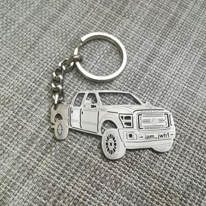 May include: Silver-colored truck-shaped keychain with a chain and ring. The keychain features a detailed outline of a pickup truck with visible wheels, headlights, and a grille. The text "iam_jwh1" is visible on the front.