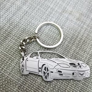 May include: A silver keychain featuring a detailed cutout of a black sports car. The keychain has a silver ring and a chain.
