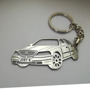 Puede incluir: Llavero de plata con un recorte detallado de un Lincoln Town Car con el nombre "JOEY B" grabado en la matrícula.