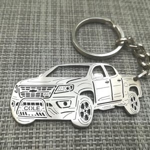 May include: Silver metal keychain featuring a detailed outline of a Chevrolet Colorado pickup truck with the name "COLE" engraved on the number plate.