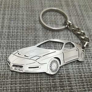 May include: Silver keychain featuring a detailed cutout of a sports car with the text "J_SOSA" on the front.