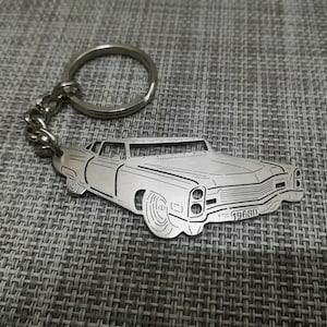 Może przedstawiać: Srebrny metalowy brelok do kluczy z wyciętym detalicznie klasycznym samochodem z nadrukowanym rokiem 19680 na tablicy rejestracyjnej.