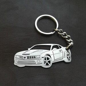 May include: A silver metal keychain featuring a detailed outline of a Chevrolet Camaro. The keychain has a silver metal ring and chain.