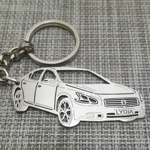 May include: Silver car keychain with a detailed outline of a sedan and the name "LYDIA" engraved on the license plate.