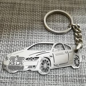 May include: A silver keychain featuring a detailed cutout of a silver car with the license plate "KSLJ3".