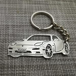 May include: Silver keychain featuring a detailed outline of a car with the name "Kelan" engraved on the front.