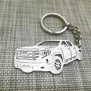 May include: Silver metal keychain featuring a detailed outline of a GMC pickup truck. The truck has the GMC logo and the text "LaBestia" on the front.