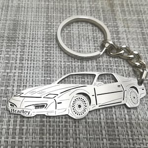 Puede incluir: Llavero de metal plateado con un contorno detallado de un coche deportivo con el nombre "Bradley" grabado en la parte delantera. El llavero tiene un anillo de metal plateado.