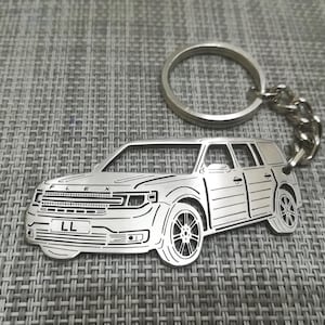 May include: Silver metal keychain featuring a detailed outline of a Ford Flex SUV. The keychain includes a silver ring and chain. The car has the word "FLEX" and the letters "LL" on the front.