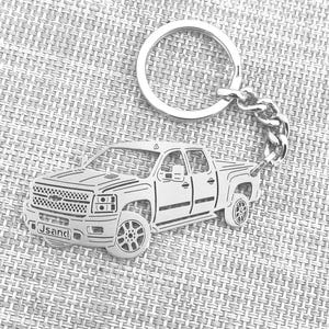 May include: Silver-colored keychain featuring a detailed outline of a pickup truck. The keychain includes a ring and chain for attaching keys. The truck design has intricate details, including the grille, headlights, and wheels. The text "Jsandl" is visible on the front of the truck.