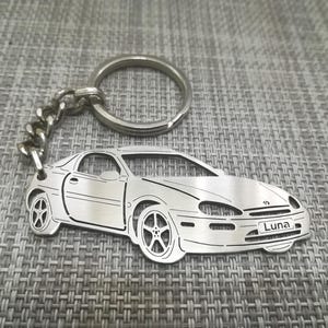 May include: Silver keyring featuring a detailed cutout of a car with the name "Luna" engraved on the number plate.